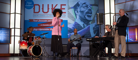 band on stage with woman singing and guitar, saxophone, drum and keyboard players 