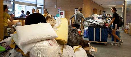 students wheel out piles of pillows and comforters, clothing, small appliances and books in bins in lobby of residence hall