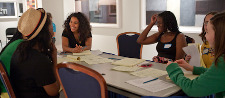 students sitting around a table with professional poet Elizabeth Acevedo, reading from poetry books during a workshop