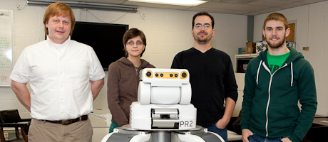 four students stand behind robot in classroom