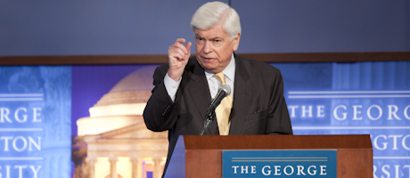 Chris Dodd speaks at podium with plaque The George Washington University. Backdrop also reads The George Washington University