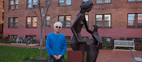 Berthold Schmutzhart stands next to sculpture of woman with a bird on her knee in University Yard