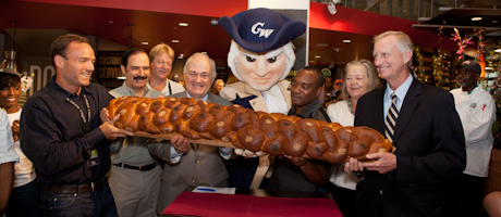Steven Knapp and mascot George stand with a group with oversized challah roll at Whole Foods opening
