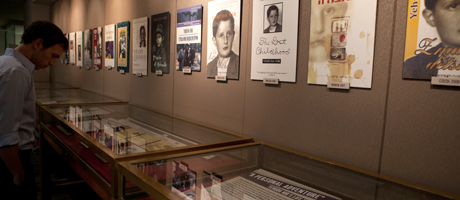 books under glass in exhibit with photographs of book covers lining walls