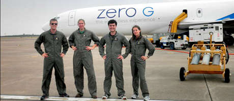 Four participants of NASA’s “Microgravity University” stand in front of “Weightless Wonder” plan in uniforms