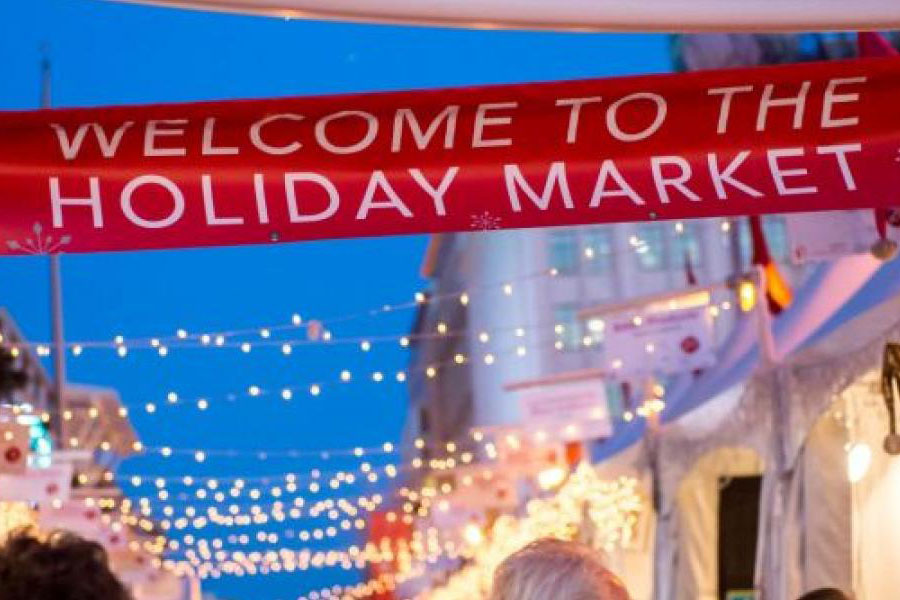 Banner strung between tents and lights reading "Welcome to the Holiday Market"