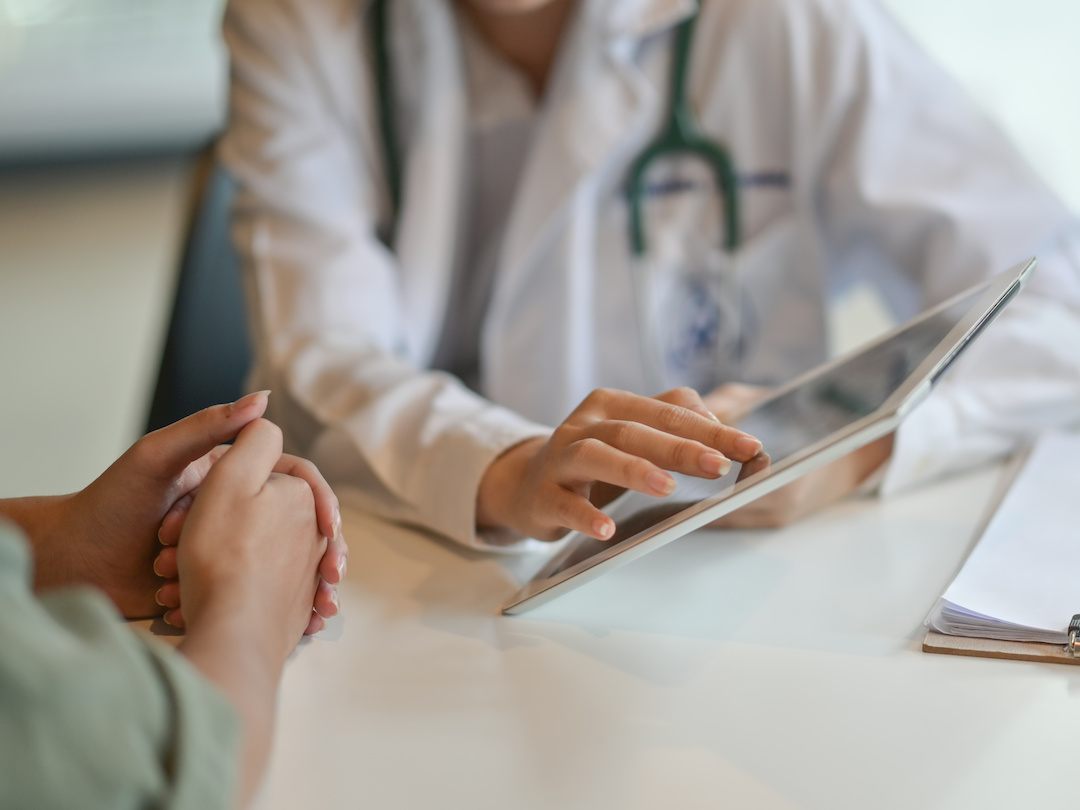 (Adobe Stock image of doctor showing patient information on tablet)