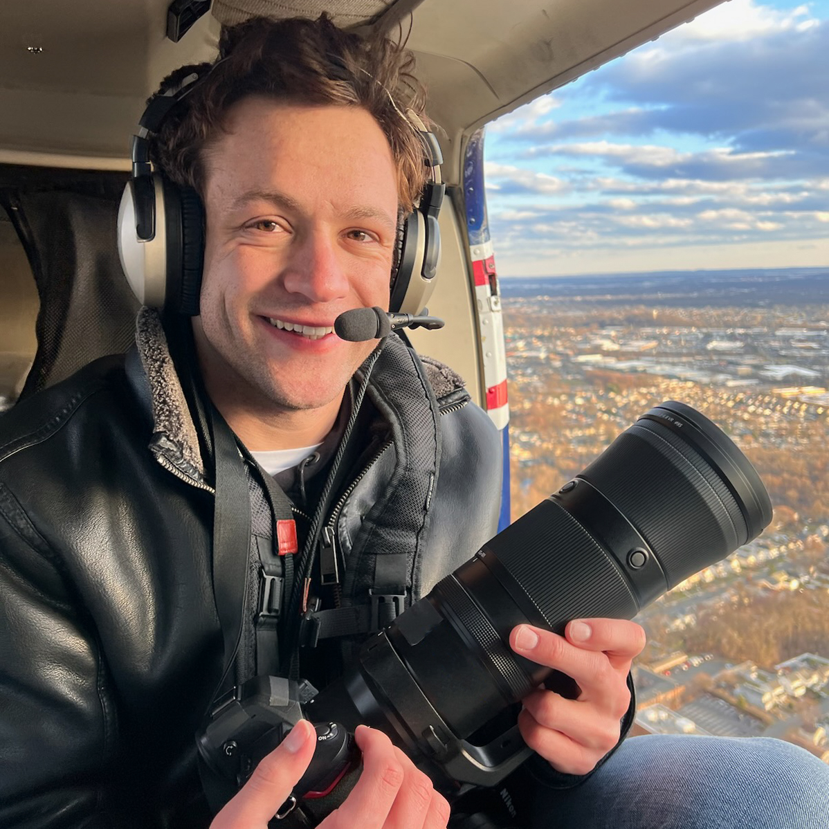 Alumnus Ryan Patterson flying in a helicopter and holding a camera.