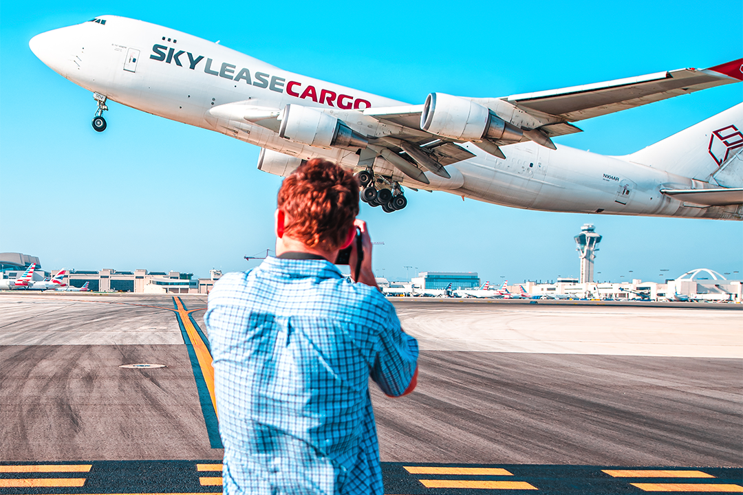 Ryan Patterson in a blue shirt with a camera taking a picture of an airplane as it takes off.