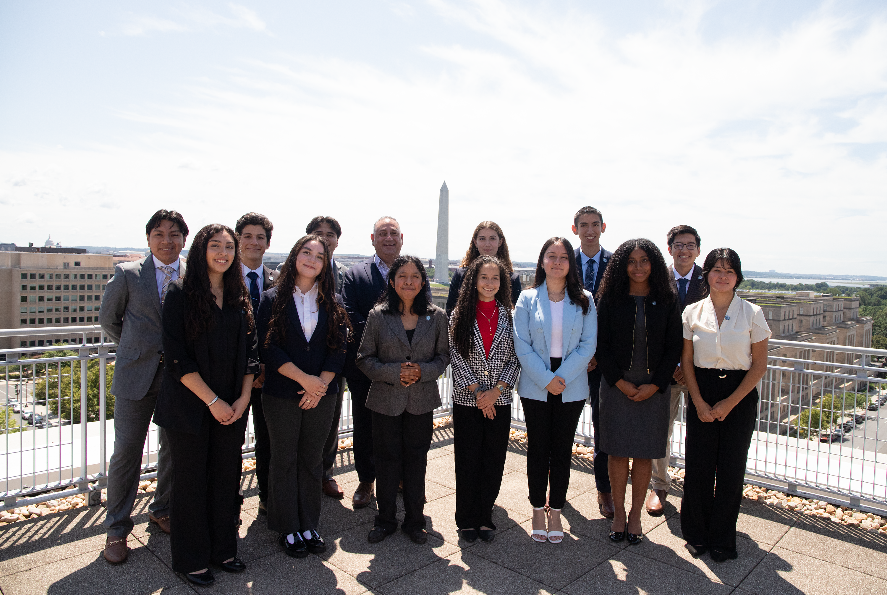 A group of Caminos al Futuro students with Gilbert Cisneros on the terrace of the City View room overlooking the Washington Monument.