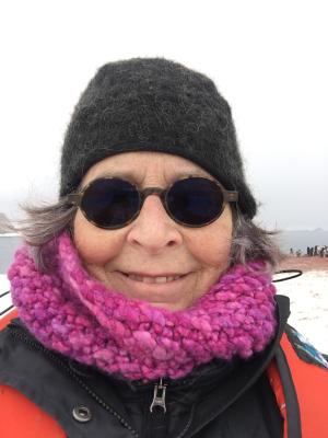 Portrait of alumna Georgeie Reynolds with a ski cap, dark glasses & pink scarf with snowy landscape in the background.
