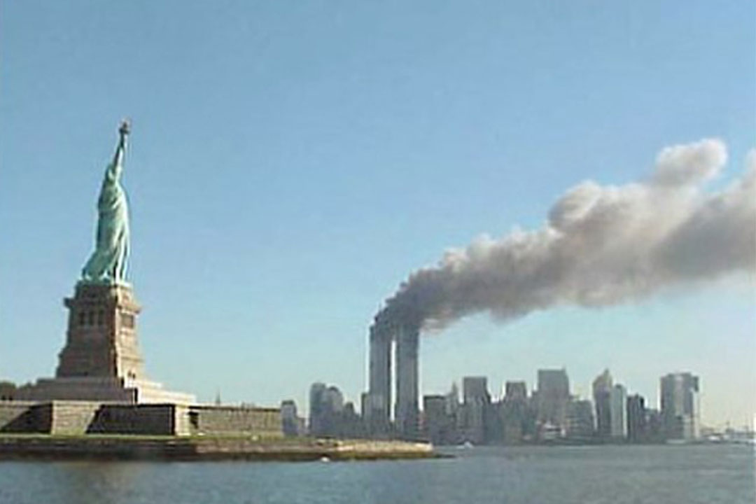 The Statue of Liberty in the New York Harbor with the World Trade Center towers smoking in the background.