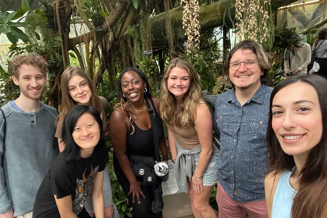 Seven biology students smiling at the camera in front of trees at the Botanic Garden.
