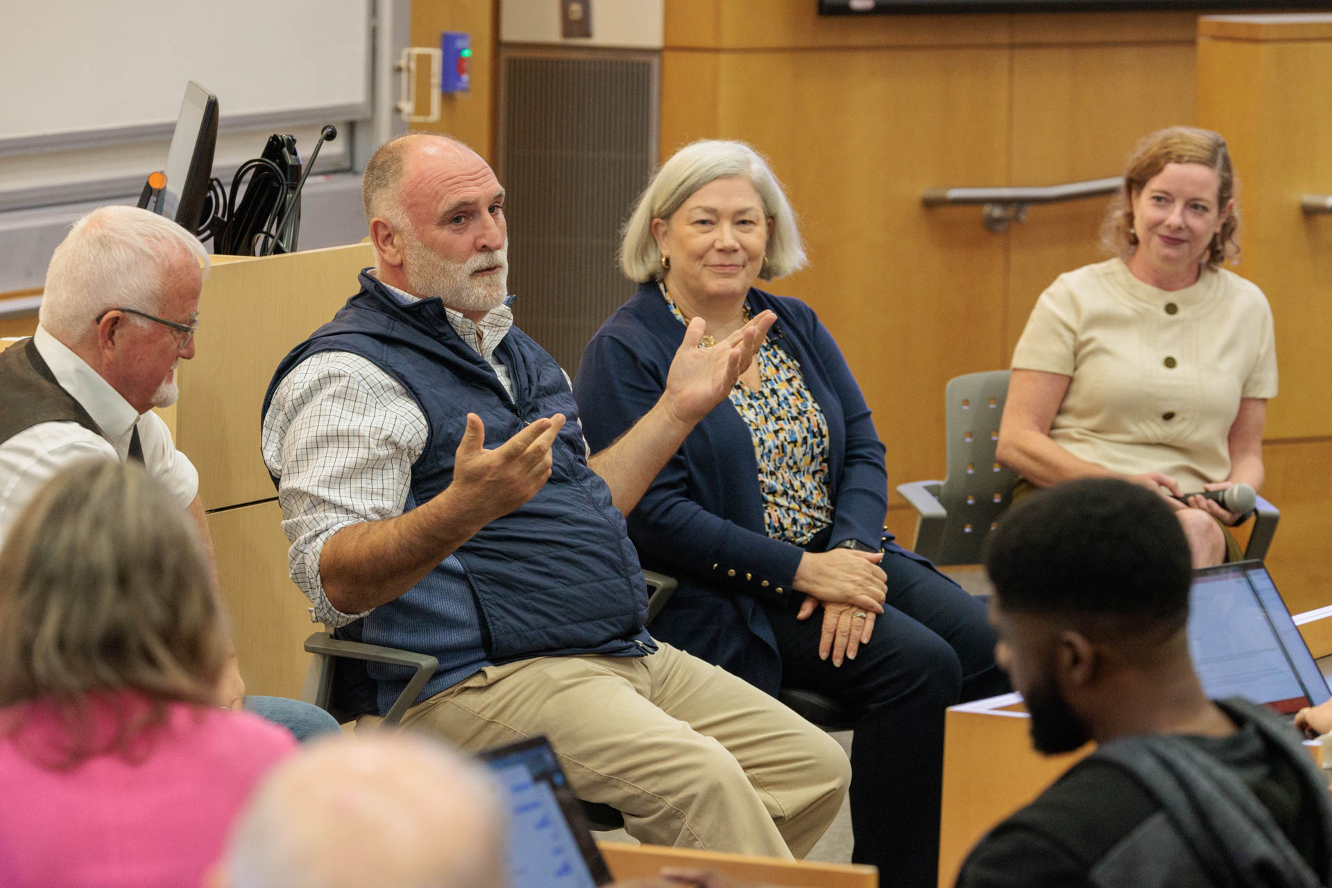 Jose Andres in a vest with hnads out speaking to a class with Robert Eggers on his right and President Granberg and Tara Scully on his right.