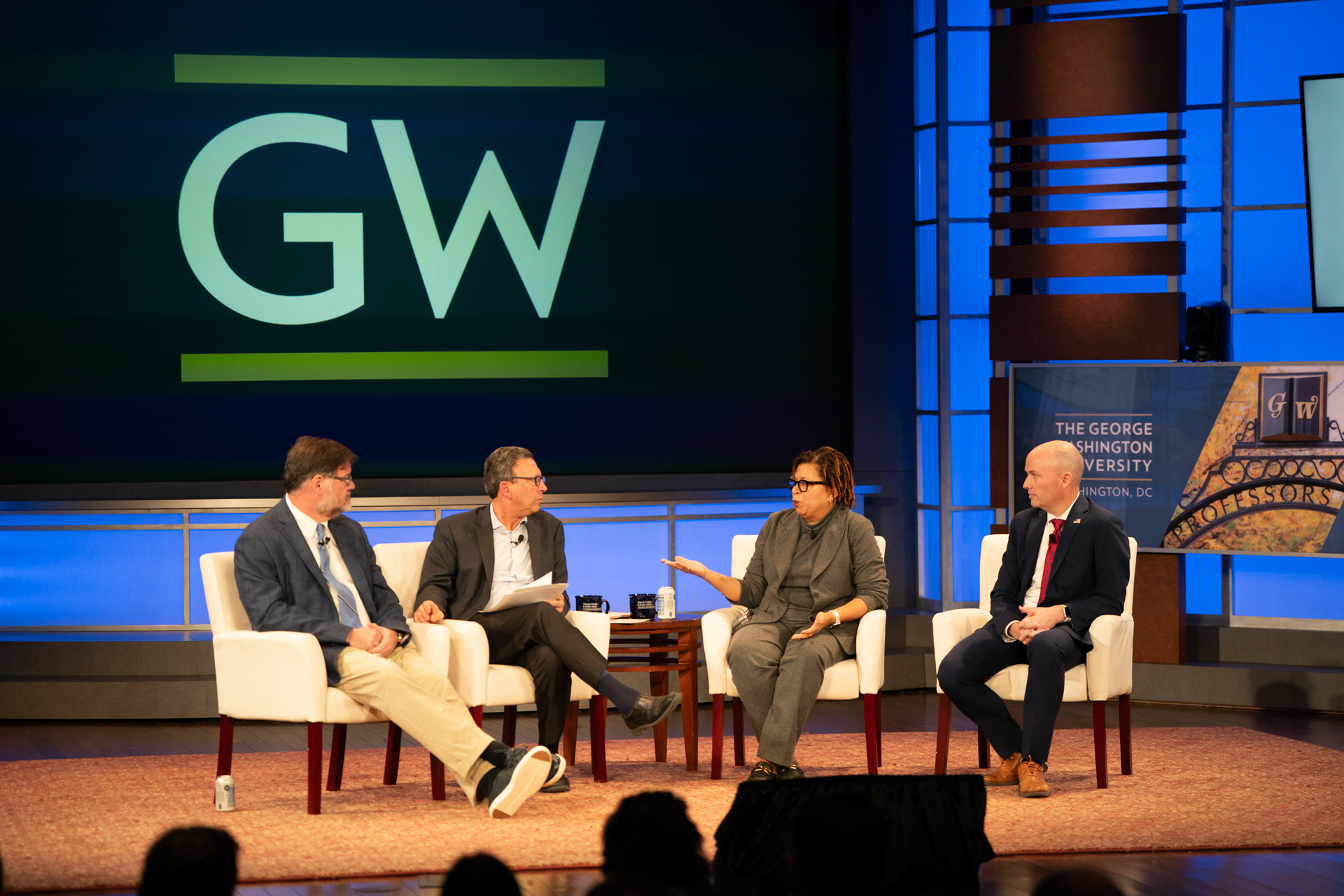 Four people talking on stage with GW logo in background.