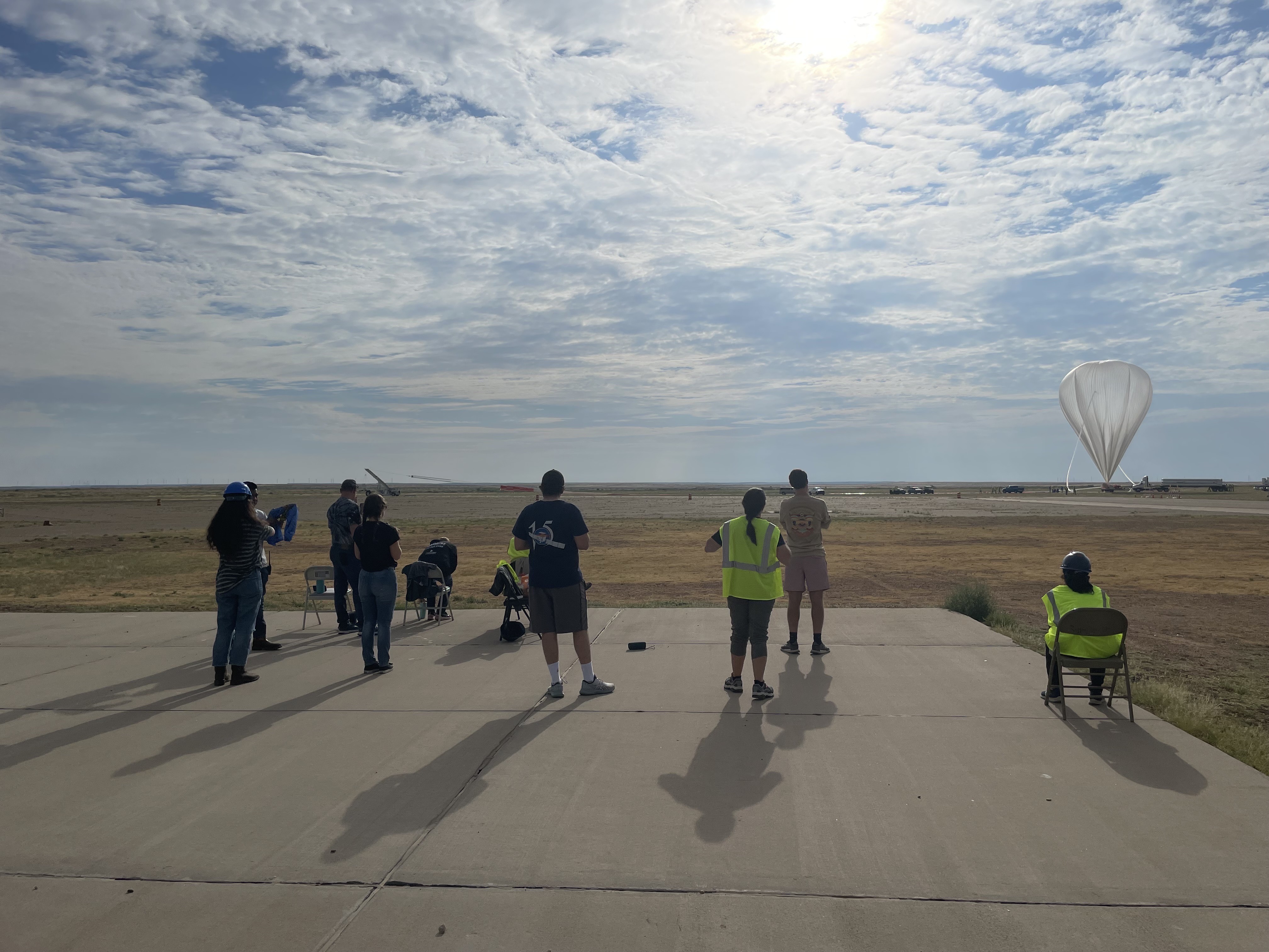 Five NASA researchers on a platform in the New Mexico desert looking into the sun with a large helium balloon about to take off