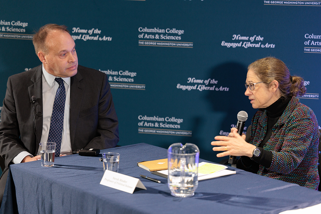 CCAS Dean Paul Wahlbeck (left) at a blue table speaking with Political Science Professor Sarah Binder