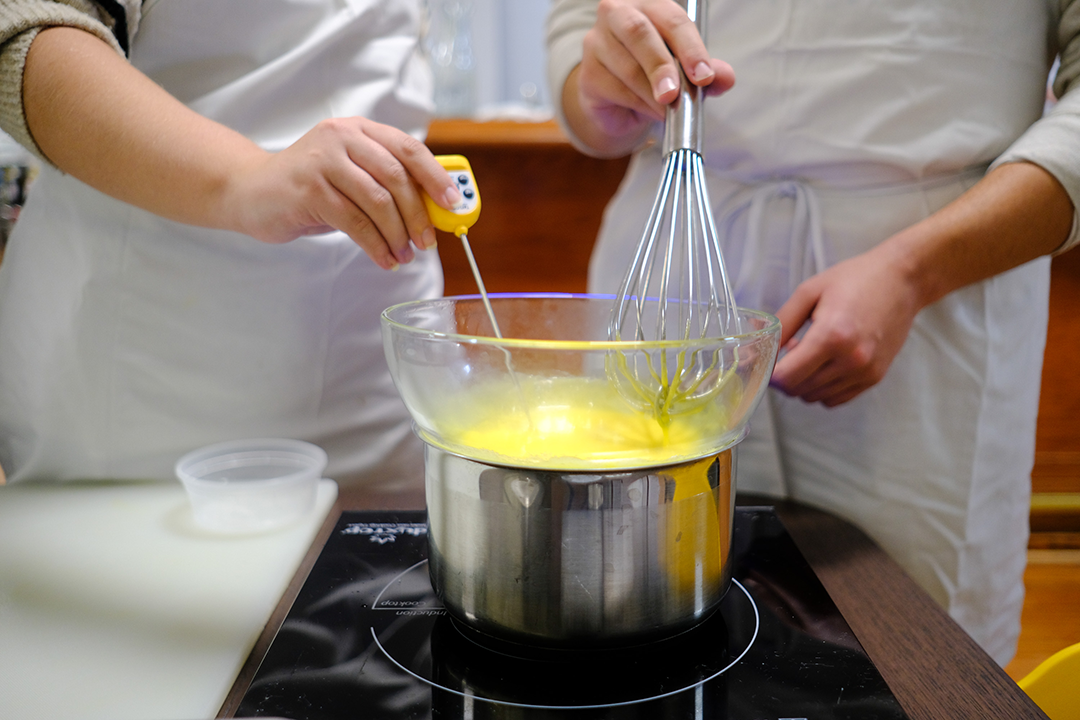 Two students hands stir a pot of custard for tiramisu