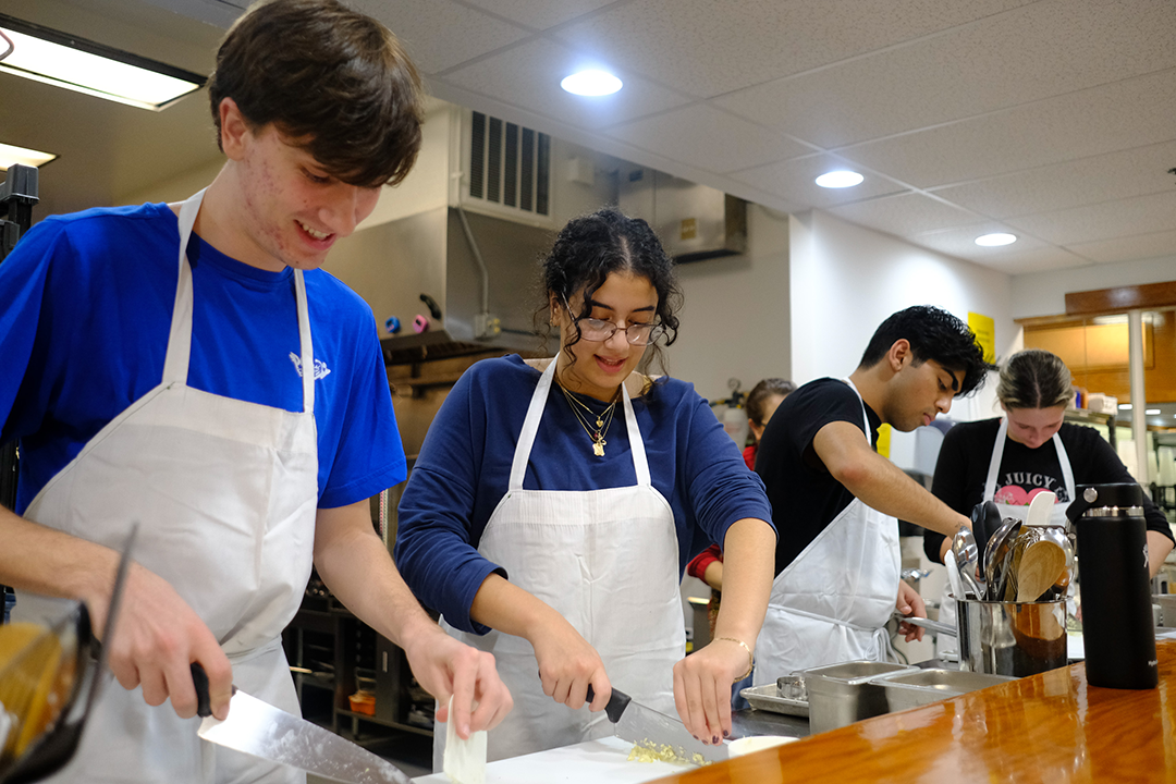 undergraduates Noah Troppe, Leana Kahwash, Krish Sadhwani and Emma Hodgson in aprons and chopping on a counter in in Italian cooking and culture class.