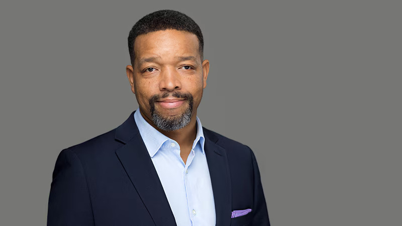 Lorenzo Norris, a man with a beard and short hair, in a navy blazer and blue shirt.. 