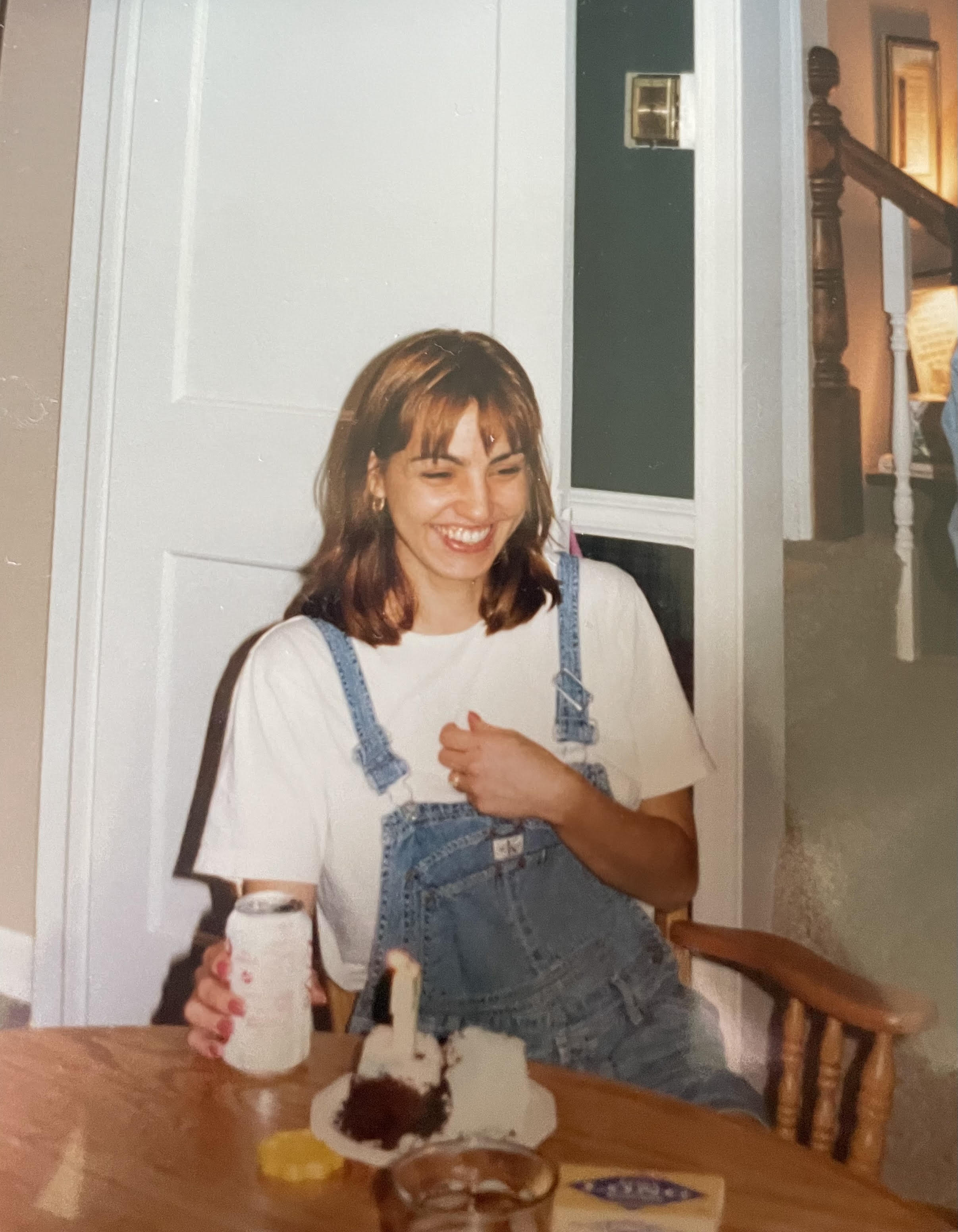 A young woman in overalls laughing with birthday cake