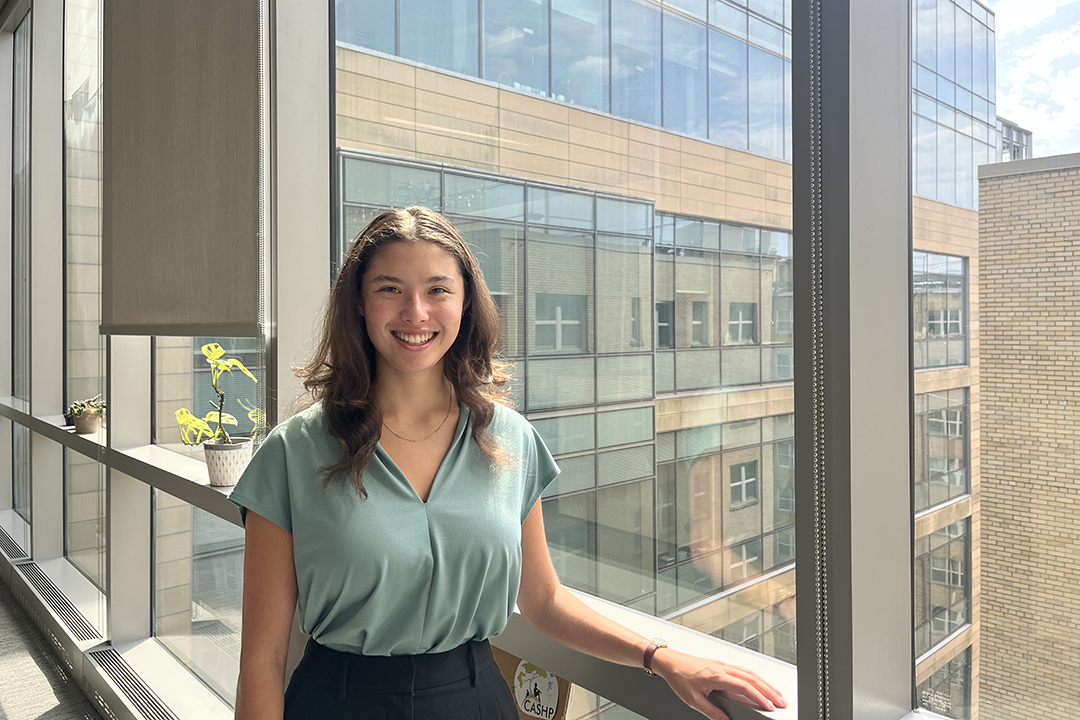 Senior anthropology major Lucia Kusta in a green blouse standing by a window
