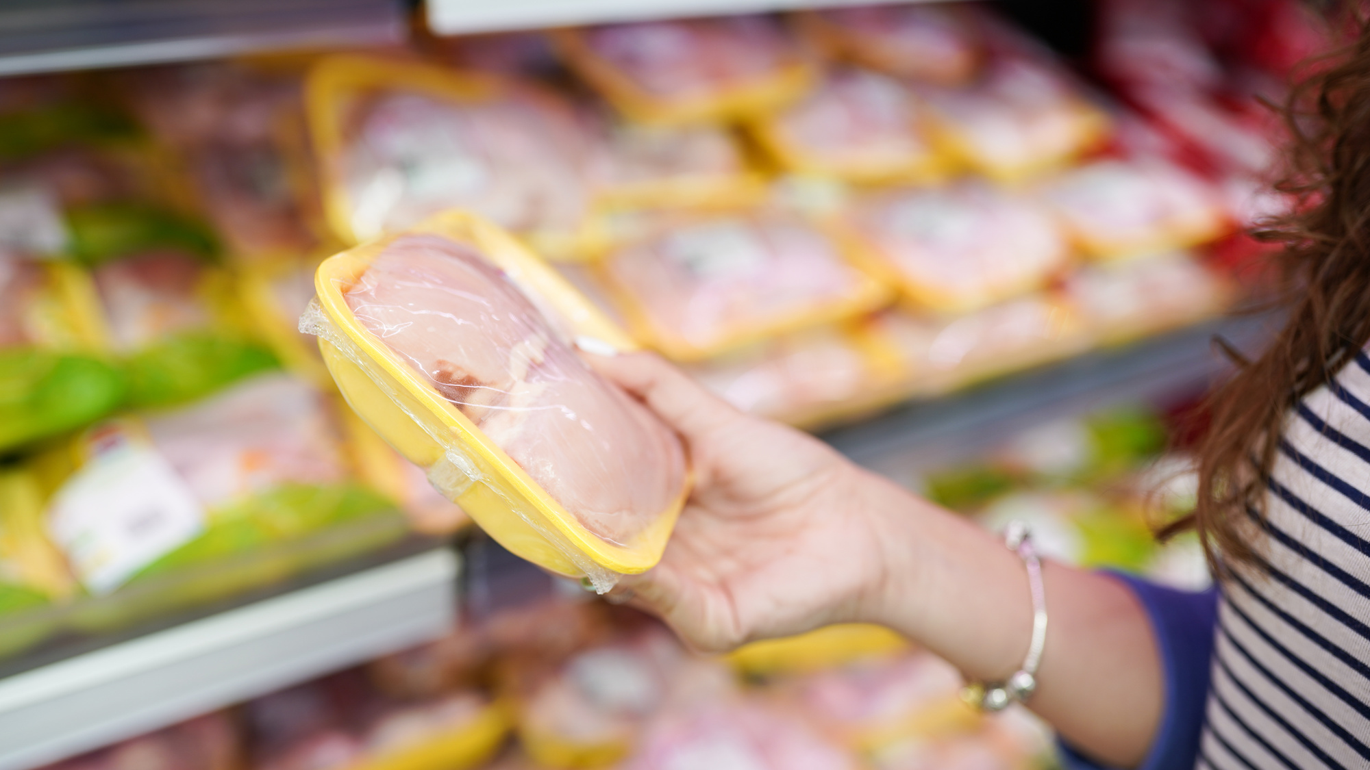 A hand holding packaged raw chicken
