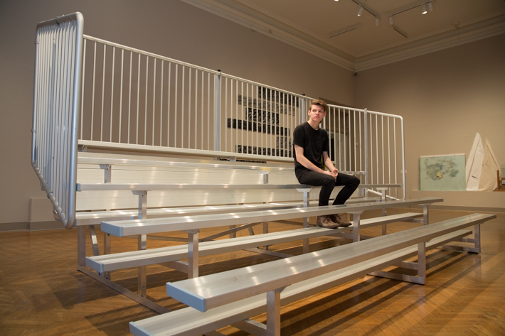 Senior Eliot Hicks, sits on the bleachers of his installation, "Versus."