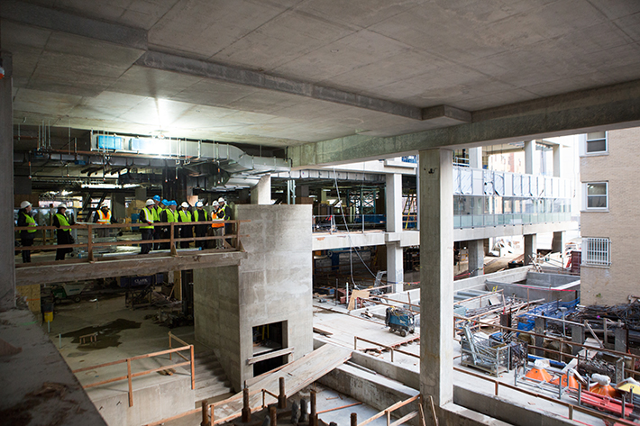 University leadership and construction members, all in hard hats, stand on a bridge at the "top out" celebration.