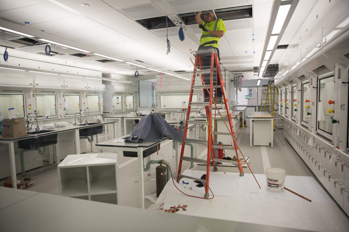 A construction worker stands on a ladder with his head poking into the ceiling of a nearly completed lab in the future Science & Engineering Hall building.
