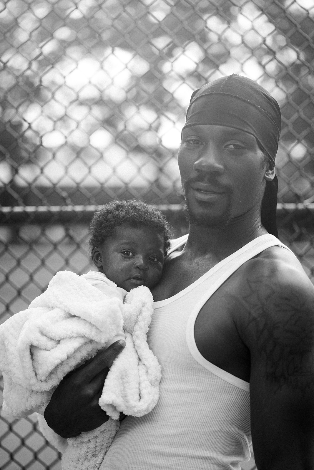 Black and white photo, a man looks at the camera while holding a baby wrapped in a blanket