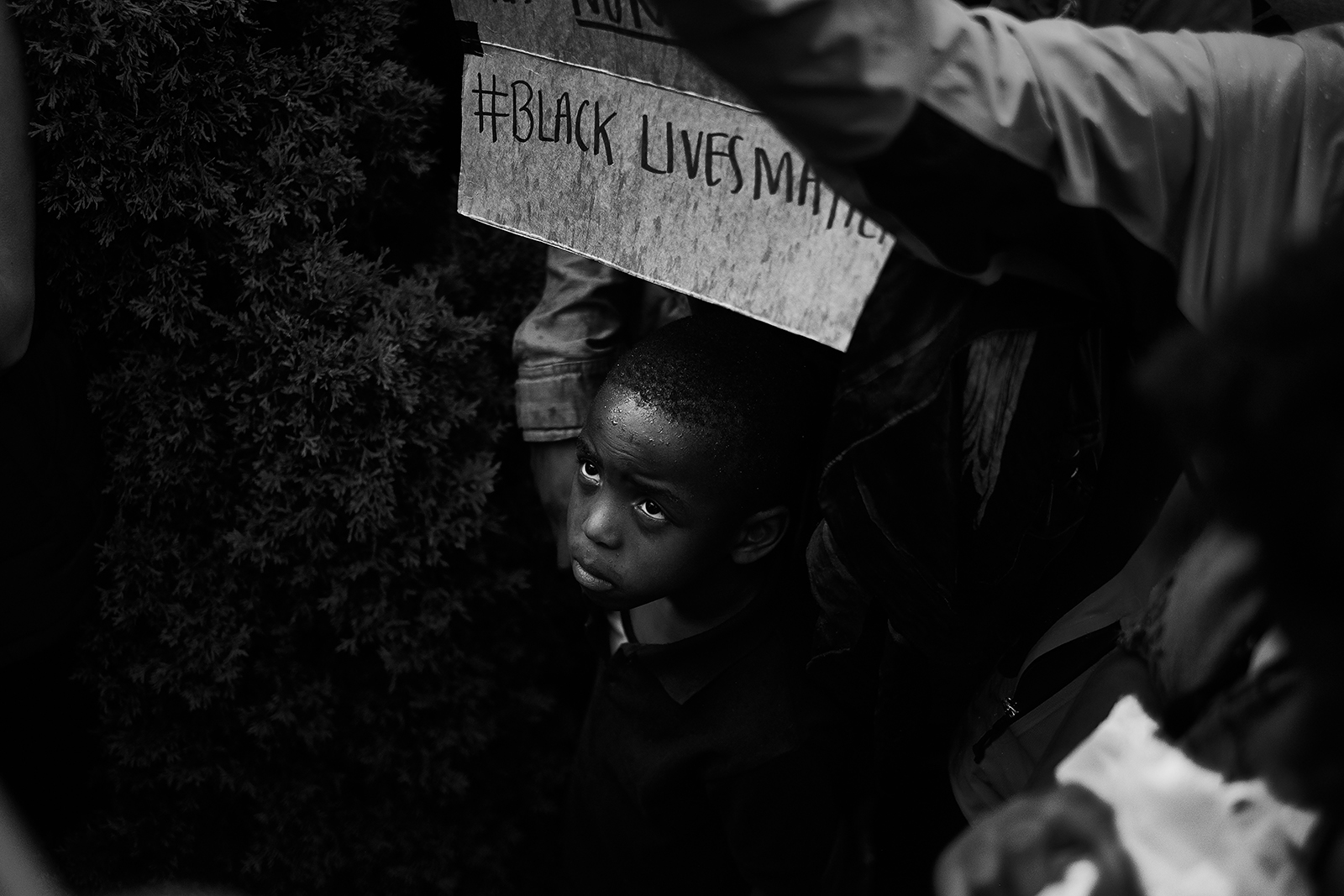 Black and white photo, small boy holding a sign that reads