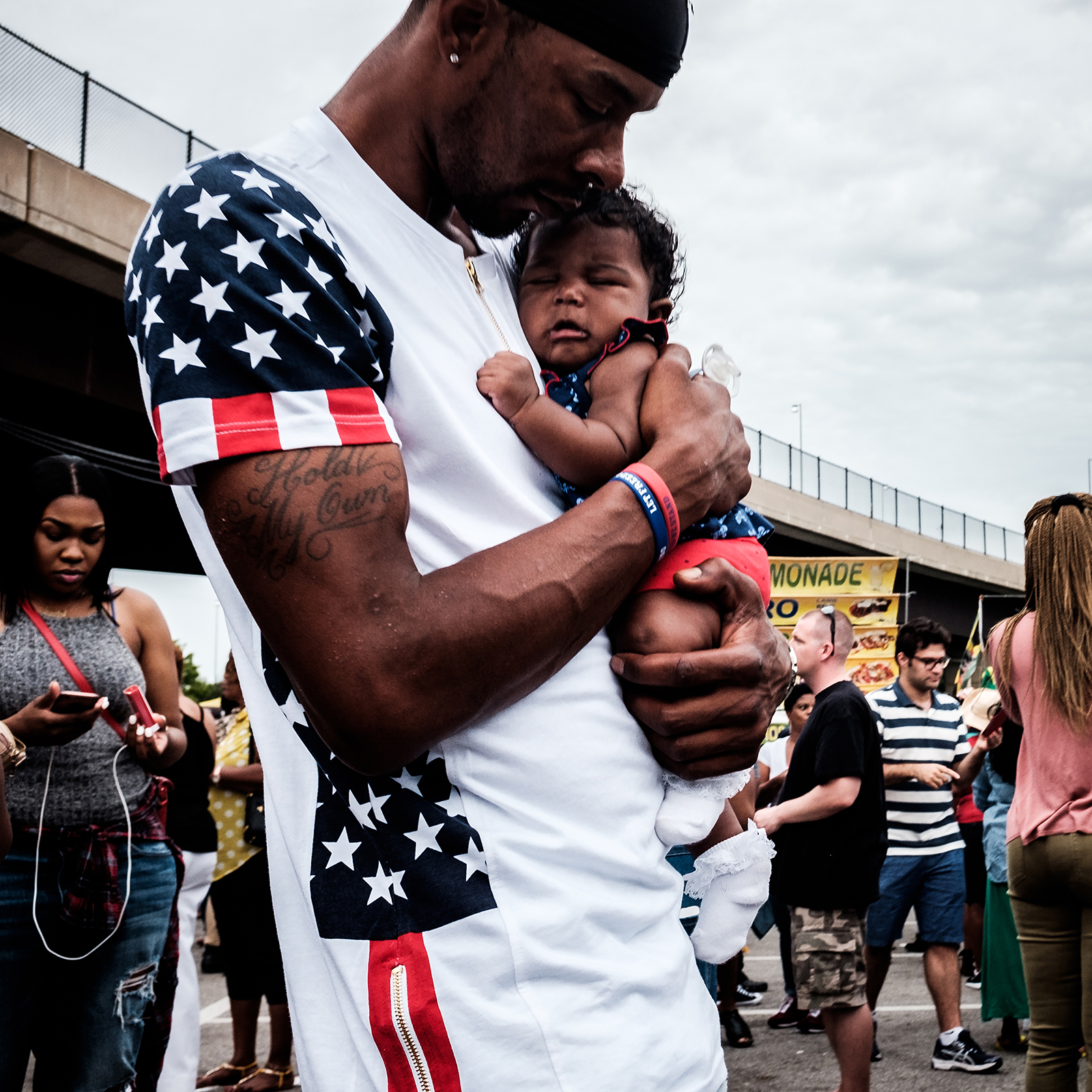 Color photo, a man in an American flag t-shirt soothes a fussy baby