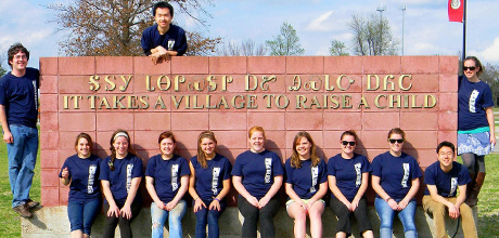 12 GW students stand in front of sign "It takes a village to raise a child"