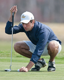 Andres Pumariega crouches down with golf club to assess next stroke
