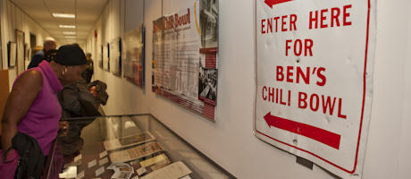 Enter Here for Ben's Chilli Bowl sign with other Ben's Chilli Bowl memorabilia behind glass with a student looking on