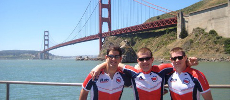 three bike riders with arms outstretched with Golden Gate Bridge in background