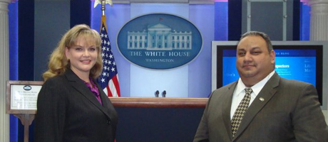 Jackie and Gilbert Cisneros smiling at White House in front of press room podium