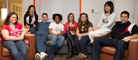 Students living in Civic House smile as a group sitting on chairs and couches