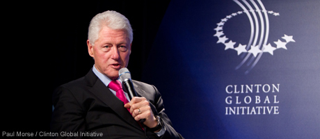 Bill Clinton speaks into microphone with Clinton Global Initiative University banner behind him