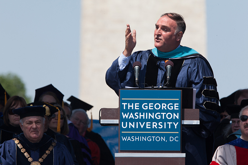 Jose Andres on commencement stage speaking at podium with Washington Monument behind him