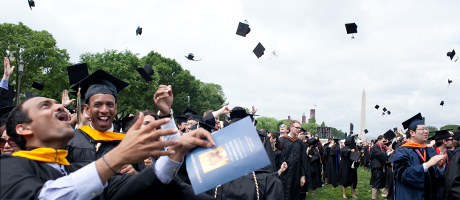students tossing graduation cpas with Washington Monument in background during commencement 