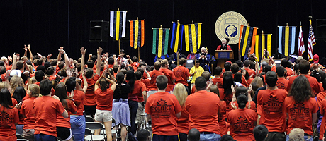 view of freshman convocation including freshmen in matching shirts and Steven Knapp in regalia at podium on stage