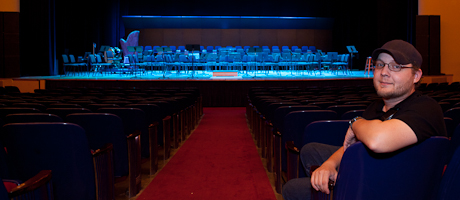 Dan Peterson sits in front of the bandshell/hardback in Lisner Auditorium with stage in background