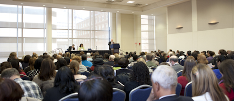 view of town hall from back of room, with seated audience and Steven Knapp speaking on stage