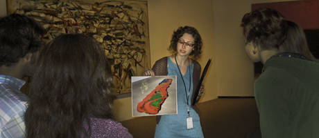 Faye Gleisser holds up a printed piece of art to a group of people in the National Gallery of Art