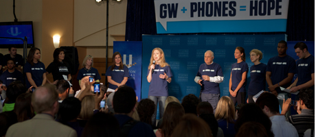 Chelsea Clinton speaks at microphone with a group on stage next to her