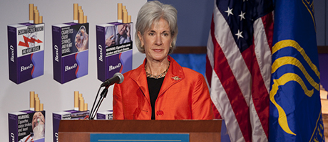 HHS Secretary Kathleen Sebelius speaks at podium with flags behind her