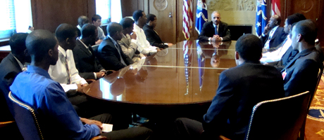 Eric Holder at head of table in DOJ with members of the basketball team sitting around the table listening