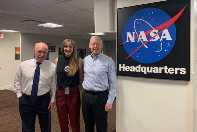 Woman between two gentlemen with NASA sign in background.